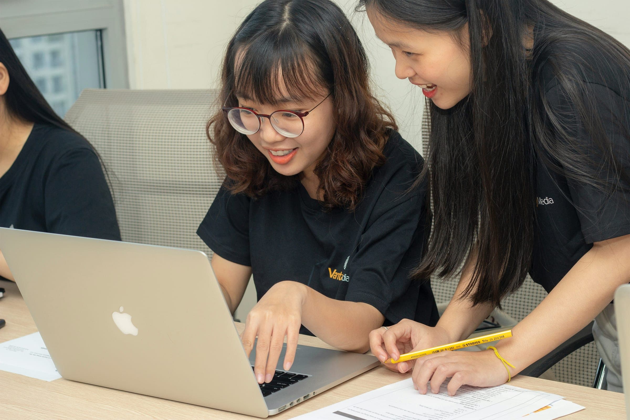 Three students collaborating around a laptop and written study materials.